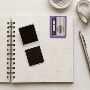 Marca-página retrô coleção Genevie com ilustração de rádio antigo roxo apoiado em caderno pontilhado aberto